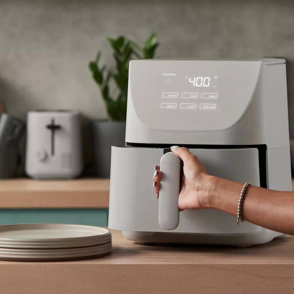 Person's hand using a modern air fryer in a kitchen setting