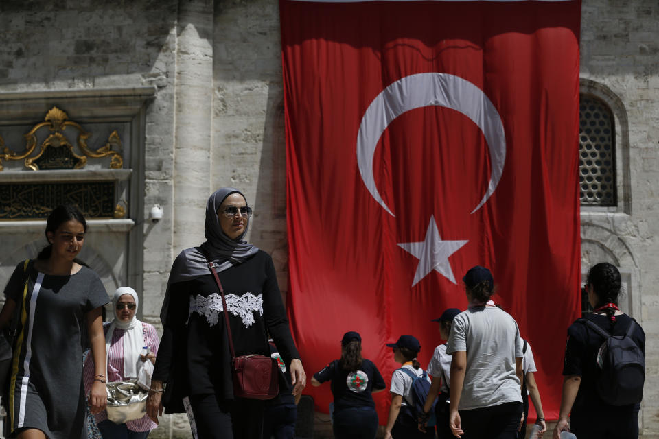 People walk past a Turkish flag on a mosque compound in Istanbul, Wednesday, Aug. 15, 2018. The Turkish government’s framing of its problems as an epic battle for sovereignty against outside enemies, particularly U.S. President Donald Trump, resonates among core supporters. (AP Photo/Lefteris Pitarakis)
