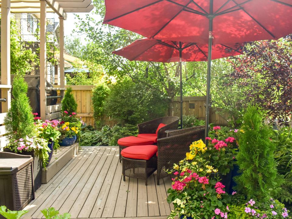 an outdoor deck surrounded by plants and greenery with a red seating area