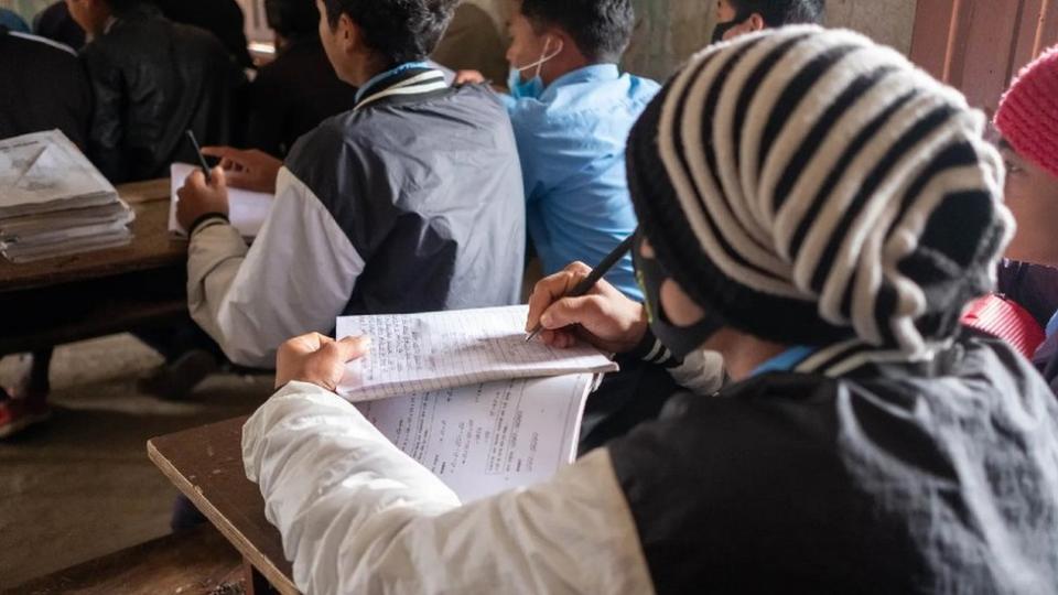 Un grupo de jóvenes, muy abrigados, estudia el kusunda en una pequeña escuela.