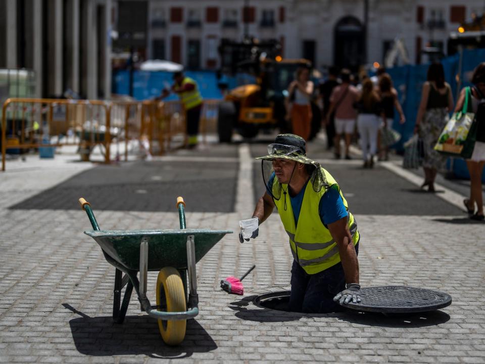 worker in yellow vest stands in manhole with cup in cobblestone street