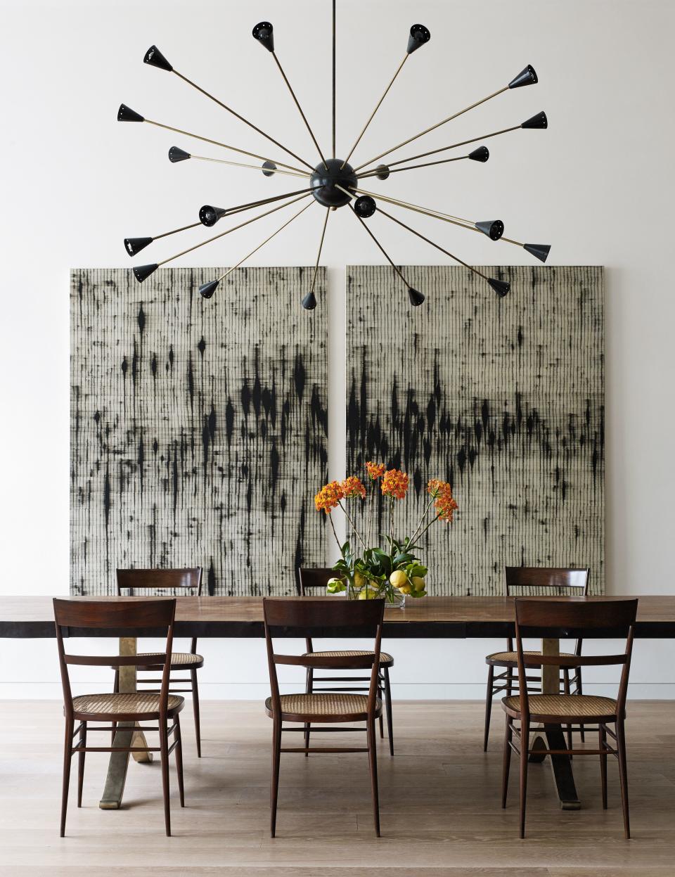 The dining table is by BDDW, and the chairs are by Joaquim Tenreiro, designed in Brazil in 1942 and purchased from R & Company. The voluminous ceiling height is purposely filled by a monumental Sputnik-style pendant from ma+39. The paintings are by Mark Francis.