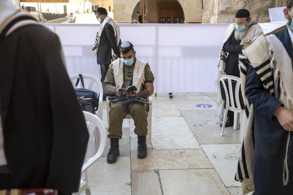 With social distancing, an Israeli soldier and ultra-Orthodox Jewish men pray ahead of Yom Kippur, the holiest day in the Jewish year which starts at sundown Sunday during a three-week nationwide lockdown to curb the spread of the coronavirus at the Western Wall, the holiest site where Jews can pray in Jerusalem's old city, Sunday, Sept. 27, 2020. The solemn Jewish holiday of Yom Kippur, which annually sees Israeli life grind to a halt, arrived on Sunday in a nation already under a sweeping coronavirus lockdown. (AP Photo/Ariel Schalit)