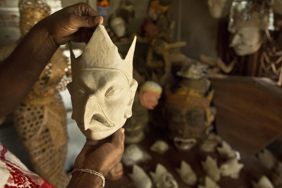 In this Tuesday, Aug. 7, 2018 photo, traditional mask maker Hemachandra Goswami holds up a mask at Samaguri Satra, a Vaishnavite monastery, in Majuli, India. Vaishnavite practice is credited with preserving the culture of mask-making, an integral part of the dance dramas or Bhaonas. At the Samaguri Satra, the monks use locally available bamboo, cane, clay, paper, jute and cow dung to shape and paint masks depicting characters from Hindu mythology. (AP Photo/Anupam Nath)