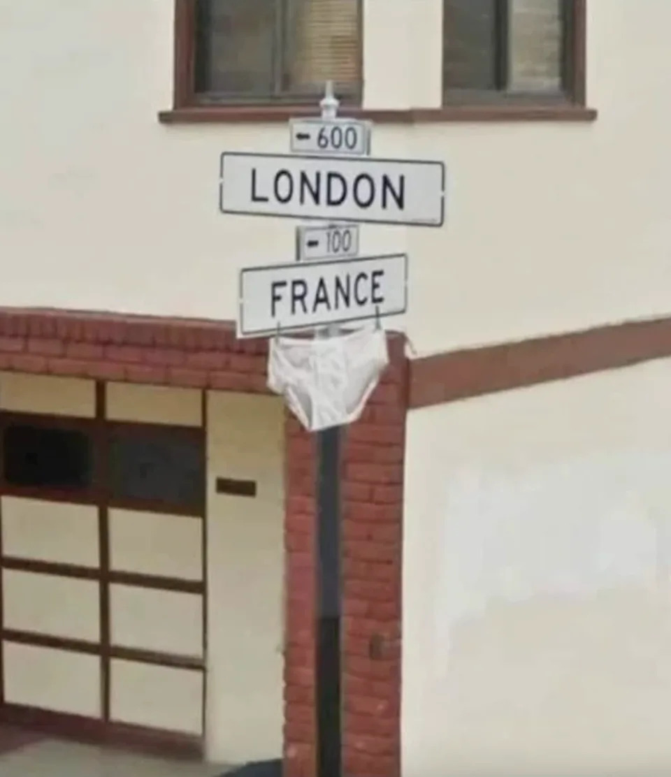 Directional signs pointing to "LONDON" and "FRANCE" with undergarments hanging on one sign