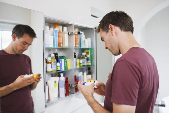 Man standing in front of open medicine cabinet, examining two prescription medicine bottles