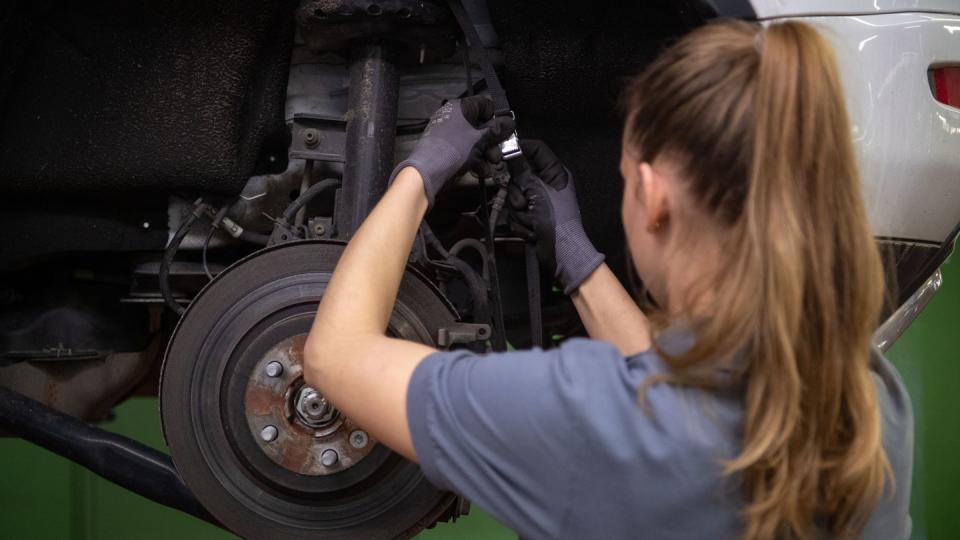 Eine KFZ-Mechanikerin wechselt in einer KFZ-Werkstatt die Bremsscheibe eines Range Rover Evoque.