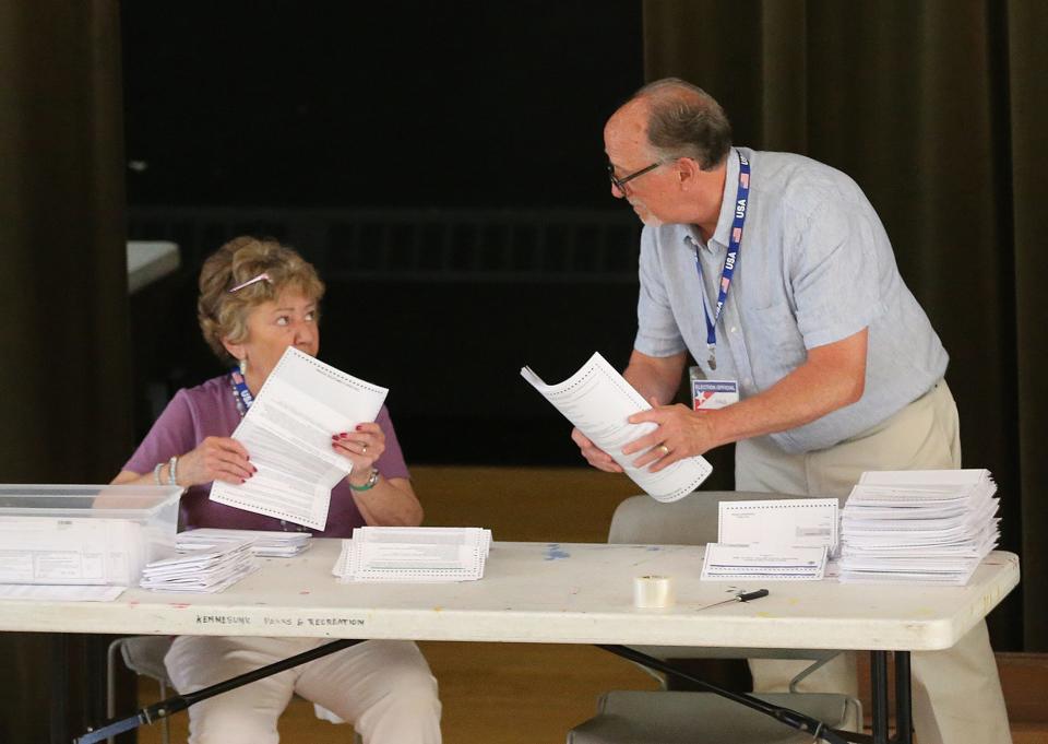 Election official Paul Coughlin speaks with another clerk as they work on absentee ballots at the Kennebunk polls June 14, 2022.