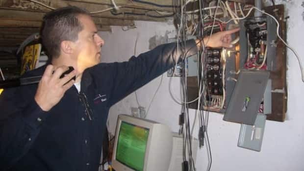 Tom Woolley checks to make sure the wires that run to the service panel are the right size for the circuit breakers or fuses in use.  (Sheila Whyte/CBC - image credit)