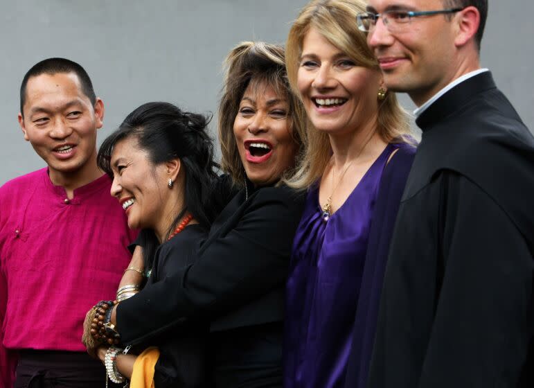 Tina Turner is wearing a black jacket, standing in a row next to Buddhist and Christian faith leaders who are smiling.