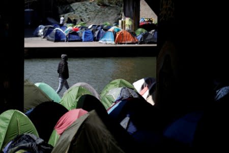 A migrant walks by the tents in a makeshift camp along the Canal Saint-Denis in Paris, France, April 6, 2018. REUTERS/Benoit Tessier