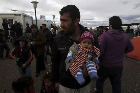 A migrant holding a child stands in a makeshift camp at the Greek-Macedonian border, near the Greek village of Idomeni March 4, 2016. REUTERS/Alexandros Avramidis