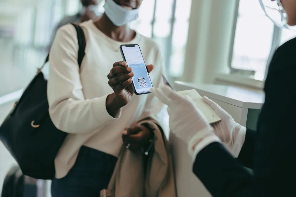 Female passenger showing medical pass to airport staff. Ground attendant checking medical pass of passenger checking in during pandemic.