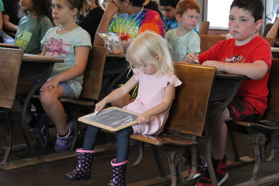 While homeschool students listen for instruction, 3-year-old Eleanor Winterholler sketches using a slate board and chalk.
