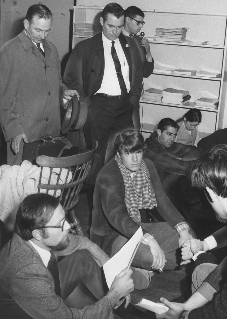 October 31, 1967: Brown graduate student Arnold Strasser reads a statement on behalf of a sit-in. Behind the students are James W. Gurll Jr. of the CIA, left, and Dean Michael J. Brennan, next to him. Dean Brennan later told the students they faced dismissal for refusing to let him pass.