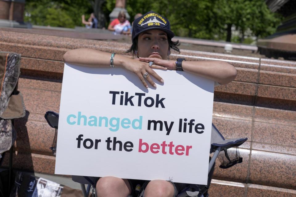 A person sitting in a folding chair with a sign reading, 