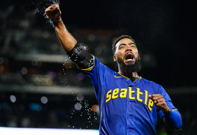 Seattle Mariners' Teoscar Hernandez holds a trident in the dugout as  teammates throw seeds at him to celebrate his solo home run against the  Kansas City Royals during the second inning of