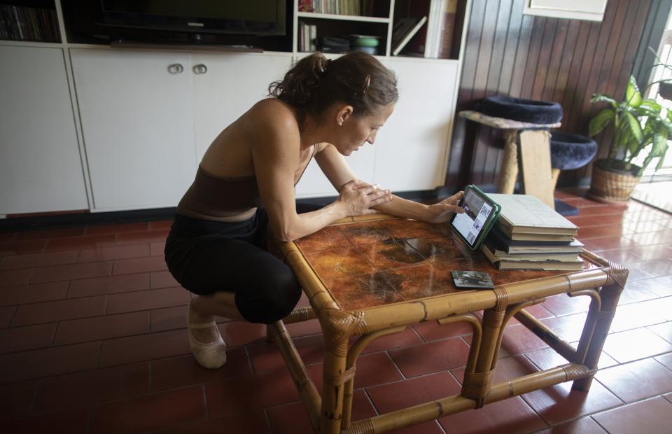 Carolina Wolf, bailarina del Ballet Teresa Carreño, busca en su tableta un video en YouTube de Ernst Meisner, del Ballet Nacional de Holanda, antes de entrenarse en la sala de su casa durante la cuarentena por la pandemia del coronavirus, el martes 11 de agosto del 2020, en Caracas. (AP Foto/Ariana Cubillos)