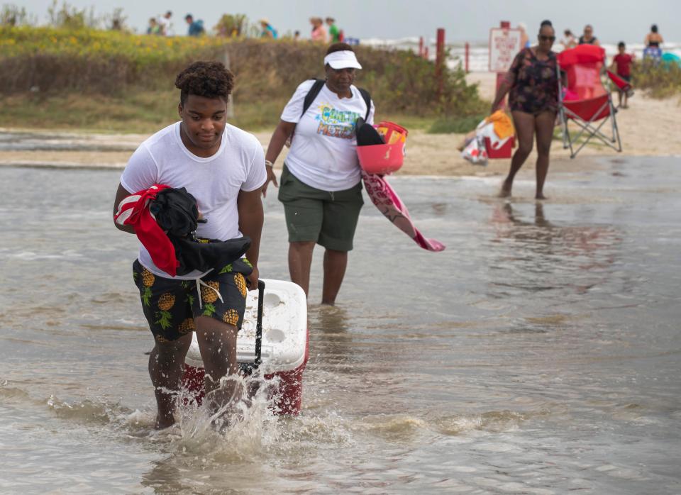 Tyler Heads totes his belongings through tidewaters as he and other beachgoers cross the flooding Stewart Beach parking lot in Galveston, Texas on Saturday, Sept. 19, 2020.