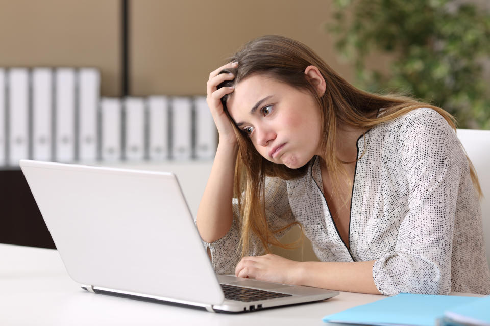 Young woman at laptop resting her head on her hand with bored expression