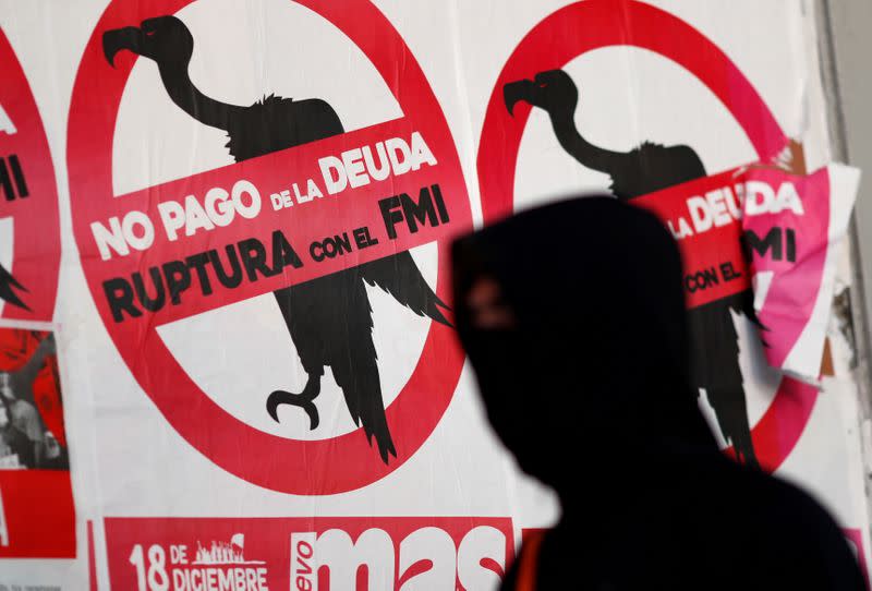 FILE PHOTO: A pedestrian wearing a face mask walks past posters on the street that read "No to the payment of the debt. Break with the IMF", in Buenos Aires