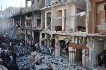 Syrian army soldiers and civilians inspect the site of two bomb explosions in the Syrian city of Homs, Syria, in this handout picture provided by SANA on December 28, 2015. REUTERS/SANA/Handout via Reuters