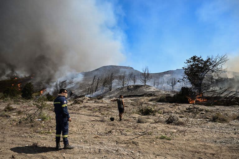 Un bombero y un civil se paran en la tierra arrasada mientras los incendios forestales queman los bosques cerca de la aldea de Vati, justo al norte de la ciudad costera de Gennadi, en la parte sur de la isla griega de Rodas el 25 de julio de 2023.