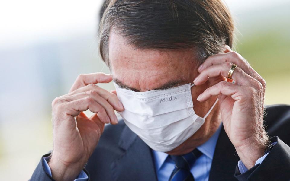 Jair Bolsonaro adjusts his face mask as he leaves his official residency in Brasilia - ADRIANO MACHADO/Reuters