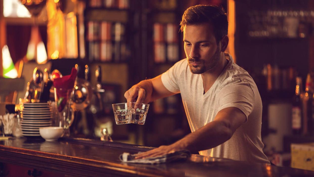 Male barista wiping and cleaning bar counter after working hours.