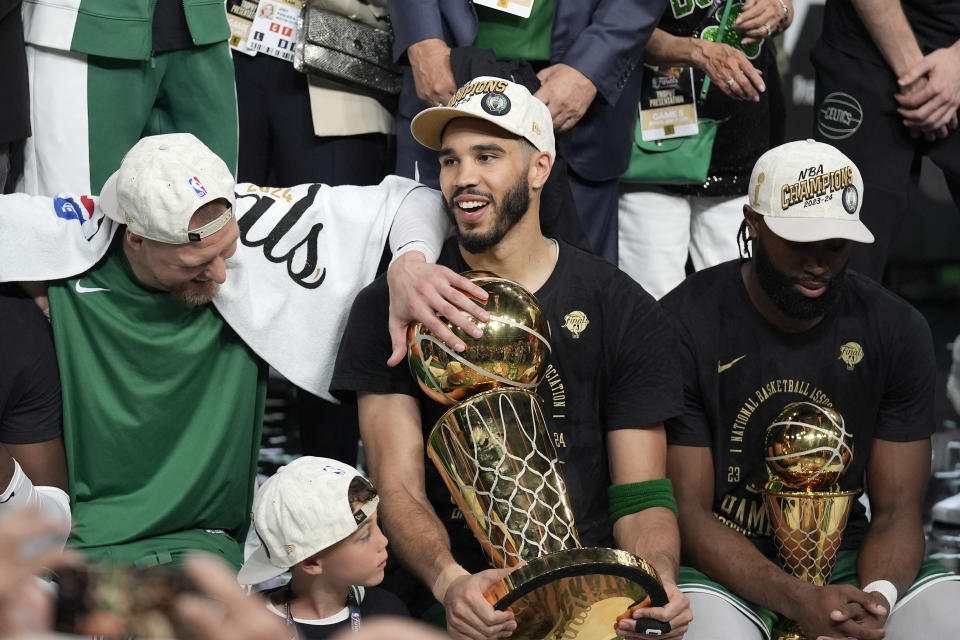 Boston Celtics forward Jayson Tatum, center, holds the Larry O'Brien Championship Trophy as he celebrates with center Kristaps Porzingis, left, and guard Jaylen Brown, right, after the Celtics won the NBA championship with a Game 5 victory over the Dallas Mavericks on Monday, June 17, 2024, in Boston. (AP Photo/Charles Krupa)