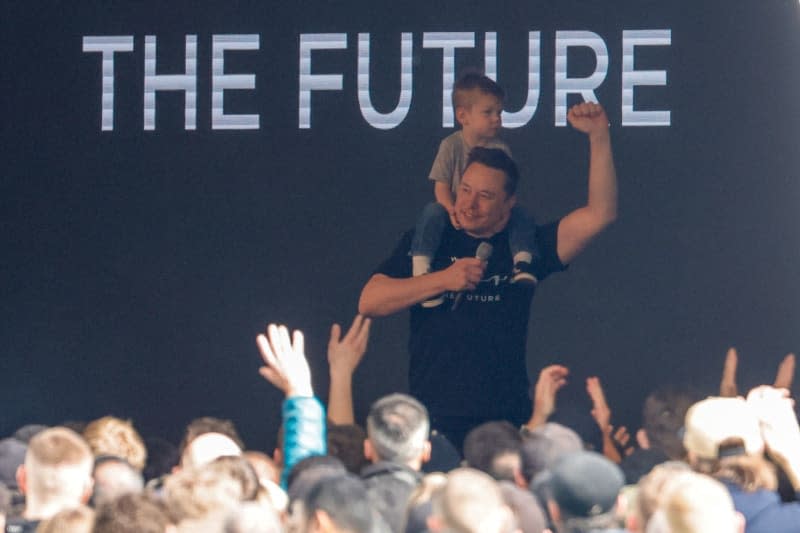 Tesla CEO Elon Musk speaks to employees at the Tesla Gigafactory Berlin-Brandenburg while holding a child in his arms. Following an attack on the electric car manufacturer Tesla's power supply, the factory is back online after a power outage lasting several days. It could take some time to ramp up production. Carsten Koall/dpa