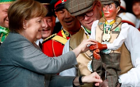 Angela Merkel touches a marionette of the "Royal Craziness" of North-Rhine Westphalia - Credit: ODD ANDERSEN/AFP/Getty Images