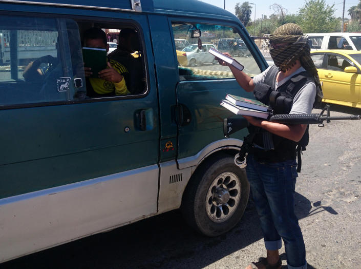 A fighter with the al-Qaida-inspired Islamic State of Iraq and the Levant (ISIL) distributes a copy of the Quran, Islam's holy book, to a driver in central northern city of Mosul, 225 miles (360 kilometers) northwest of Baghdad, Iraq, Sunday, June 22, 2014. Sunni militants on Sunday captured two border crossings, one along the frontier with Jordan and the other with Syria, security and military officials said, as they pressed on with their offensive in one of Iraq's most restive regions. (AP Photo)