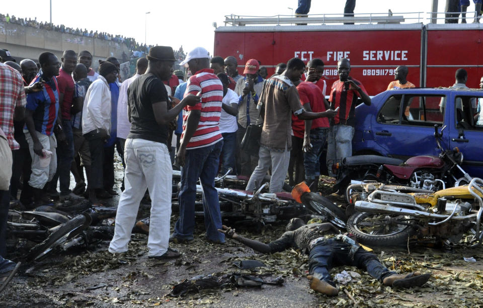 People gather at the site of a blast at the Nyanya Motor Park, about 16 kilometers (10 miles) from the center of Abuja, Nigeria, Monday, April 14, 2014. An explosion blasted through a busy commuter bus station on the outskirts of Abuja before 7 a.m. (0600 GMT) Monday as hundreds of people were traveling to work. (AP Photo/Gbemiga Olamikan)