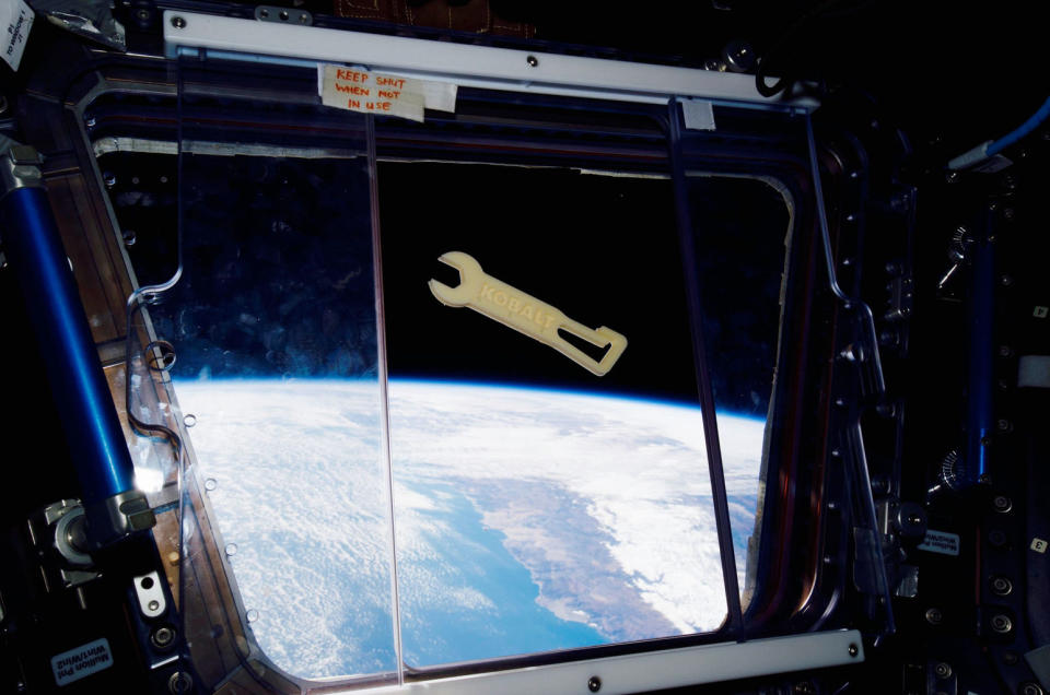 A Kobalt-branded wrench, 3D printed by Made In Space's Additive Manufacturing Facility, floats in front of a window overlooking the Earth aboard the International Space Station. <cite>Made in Space</cite>