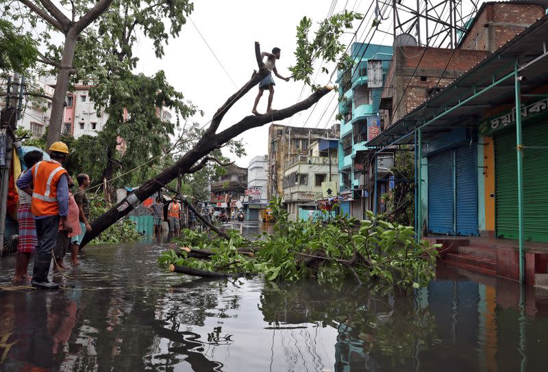 A man cuts branches of an uprooted tree after Cyclone Amphan made its landfall, in Kolkata
