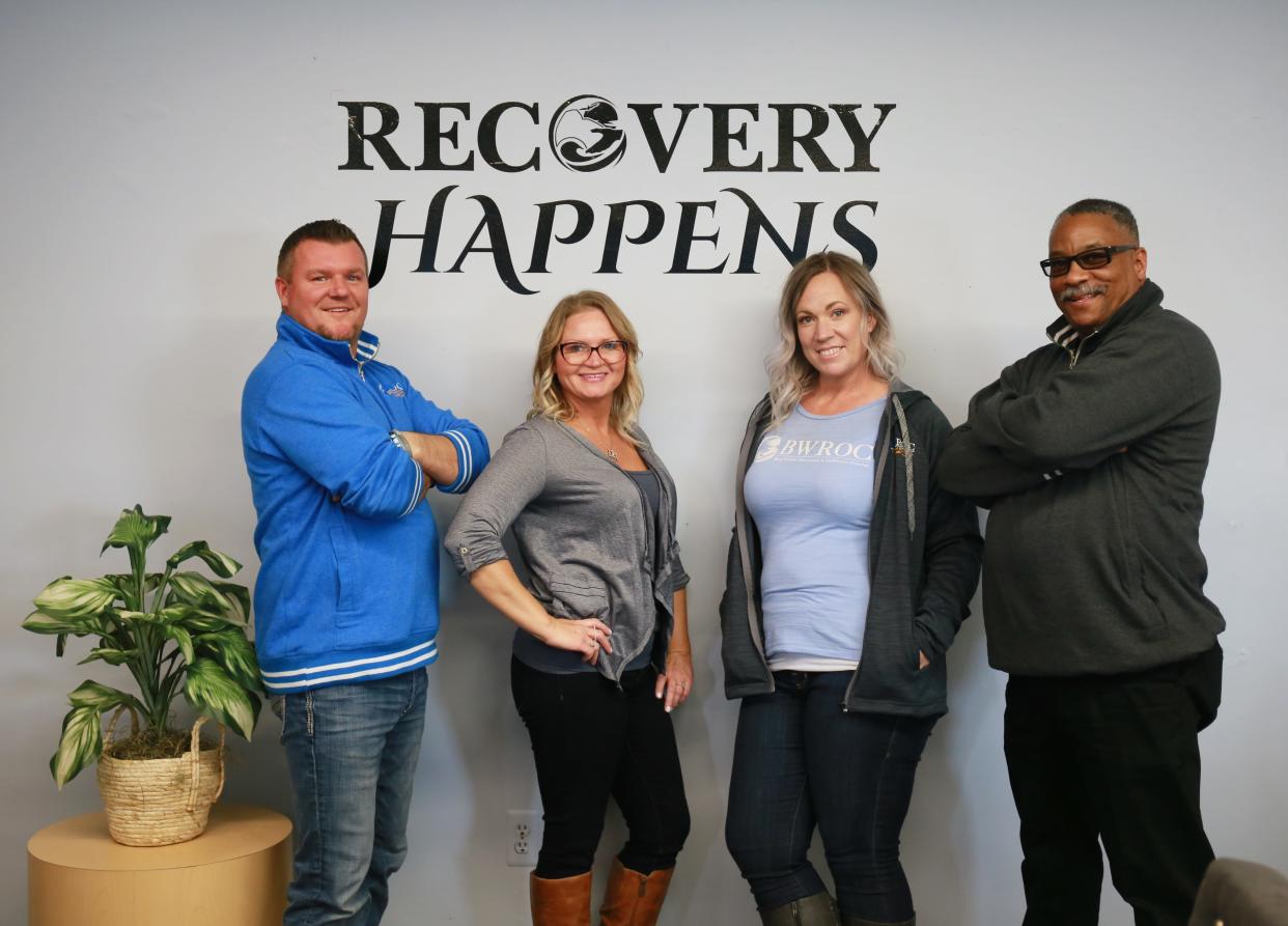Blue Water Recovery and Outreach Center staff Patrick Patterson (left), Joey Wright, Barbara Alexander, and Eric Webster stand in front of a 'recovery happens' sign on Wednesday, Feb. 9, 2022, inside the organization's center on 10th street in Port Huron.