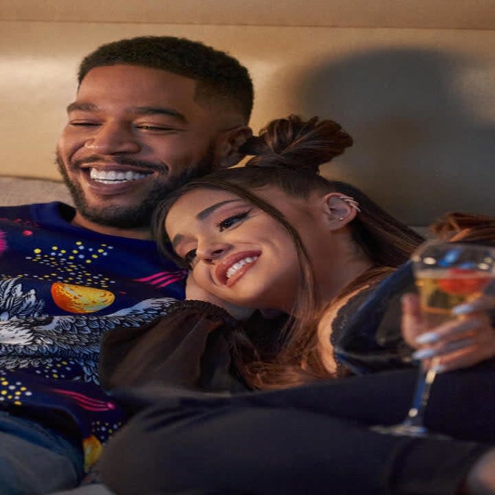 Kid Cudi with Ariana Grande sitting on a couch with glasses of champagne