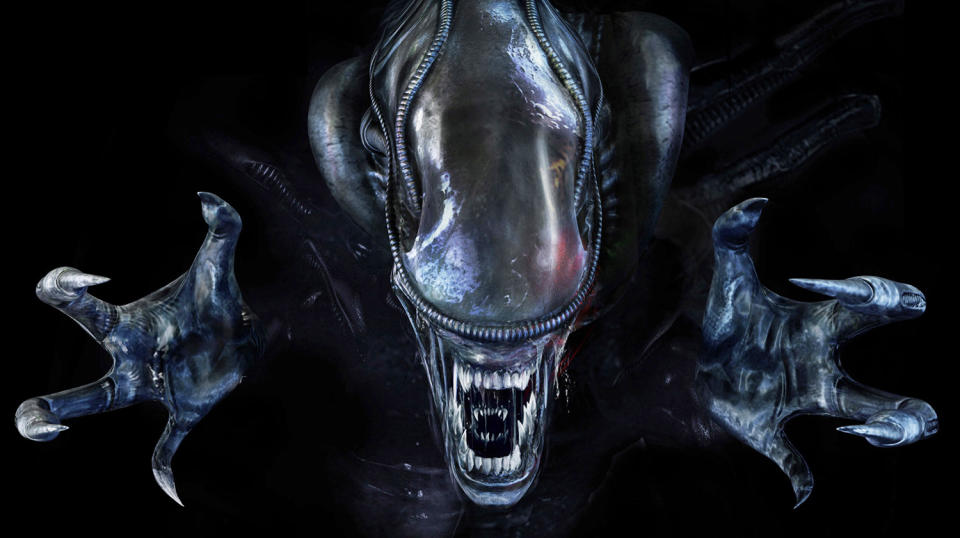 an alien with an elongated head with no eyes snarls at the viewer, baring sharp teeth