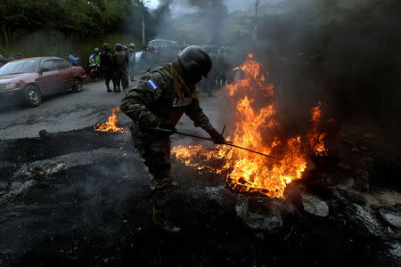 A military police officer removes a burning tire set alight by opposition supporters during a protest over a contested presidential election with allegations of electoral fraud in Tegucigalpa, Honduras, December 22, 2017. REUTERS/Jorge Cabrera