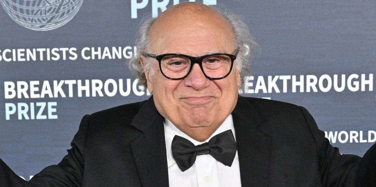 danny devito wearing a black bowtie, white shirt, a black suit jacket and trousers, and black glasses, posing on the red carpet in 2023