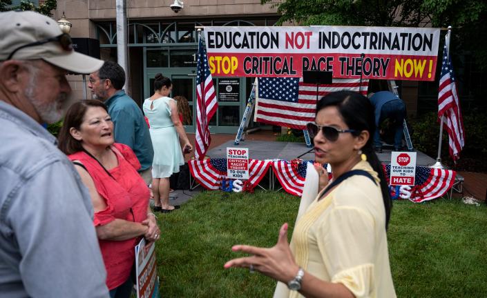People talk before the start of a rally against a banner swathed in the Stars and Stripes that reads: Education Not Indoctrination, Stop Critical Race Theory Now! 