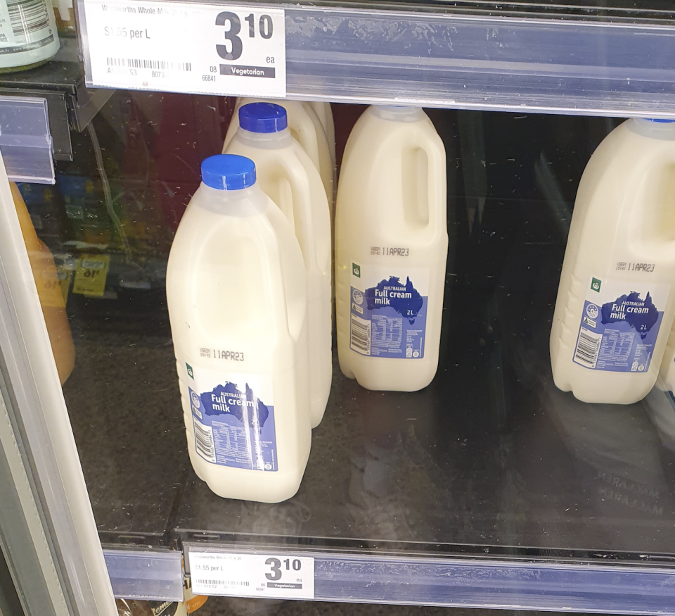 Milk sitting on a supermarket shelf with the price labelled.