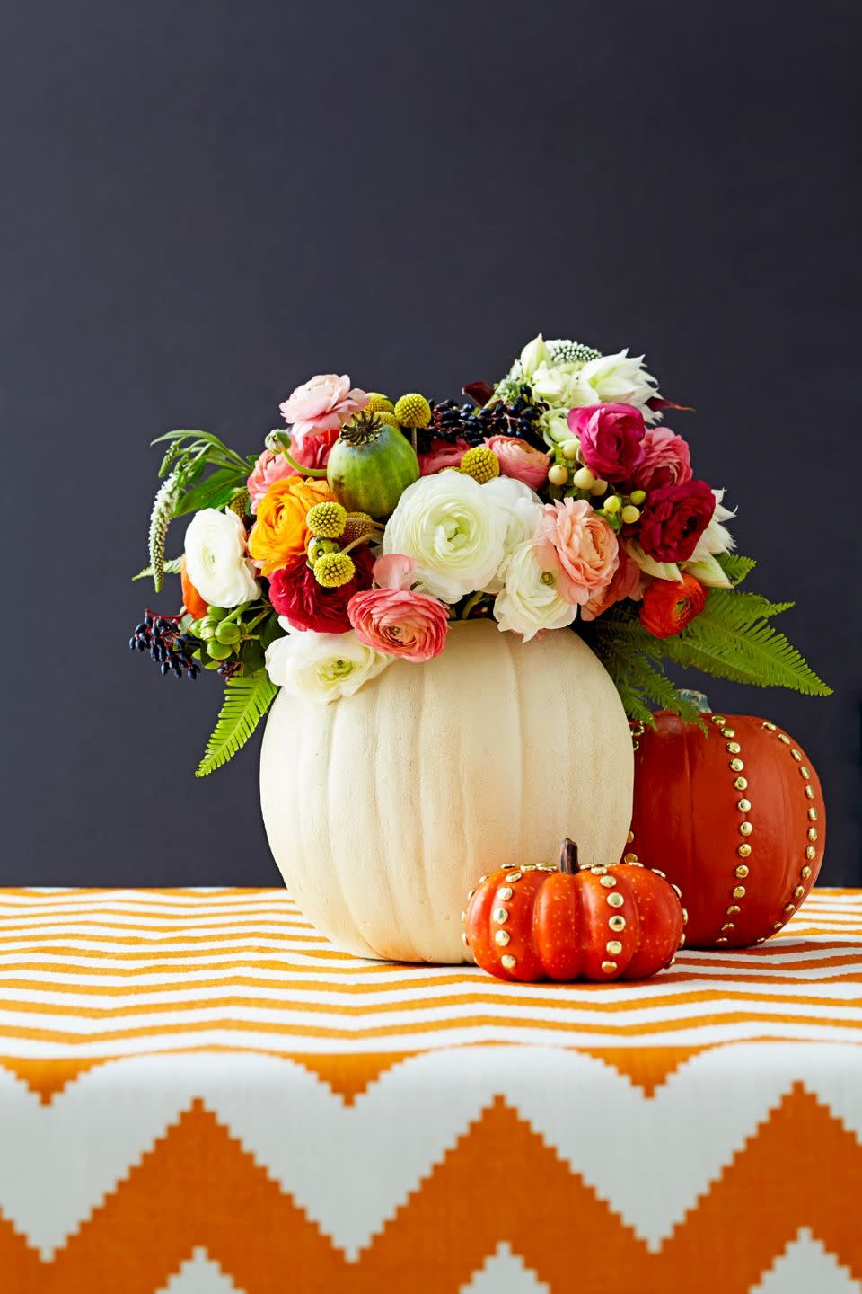 <p>Put your blooms center stage by hiding a water-filled vase inside a hollow pumpkin. Punch it up by adding shiny gold tacks along the ridges.</p>