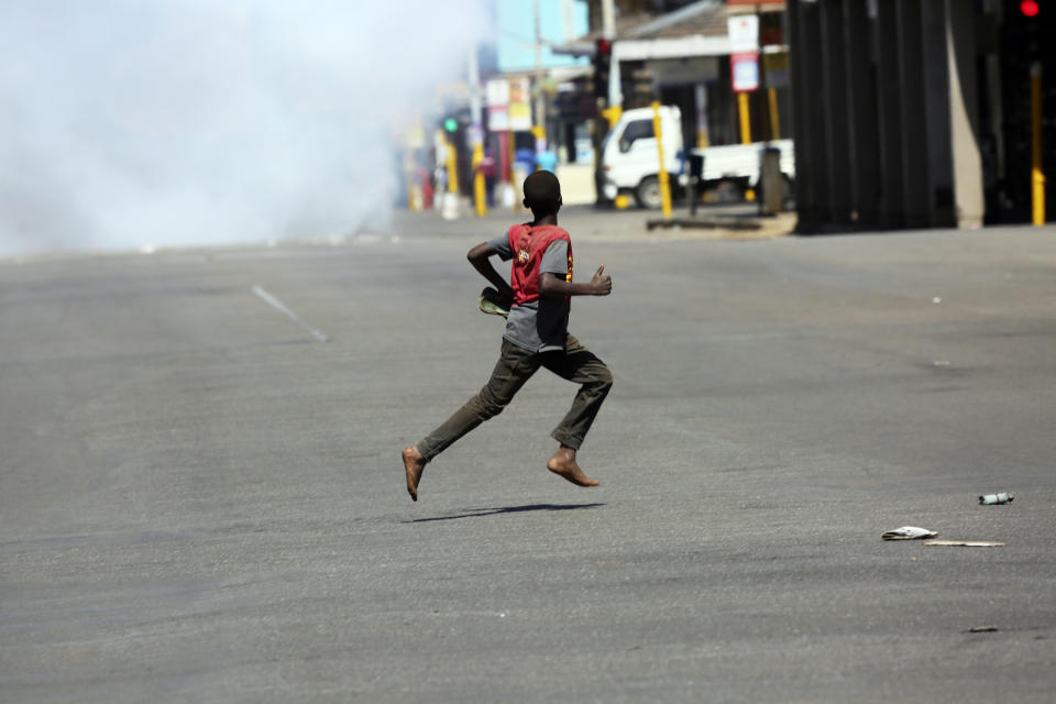 A young boy runs away from teargas during protests in Harare, Friday, Aug, 16, 2019. Zimbabwe's police patrolled the streets of Harare Friday morning while many residents stayed home and shops were shut fearing violence from an anti-government demonstration. Zimbabwe's High Court has upheld the police ban on the opposition protest.(AP Photo/Tsvangirayi Mukwazhi)