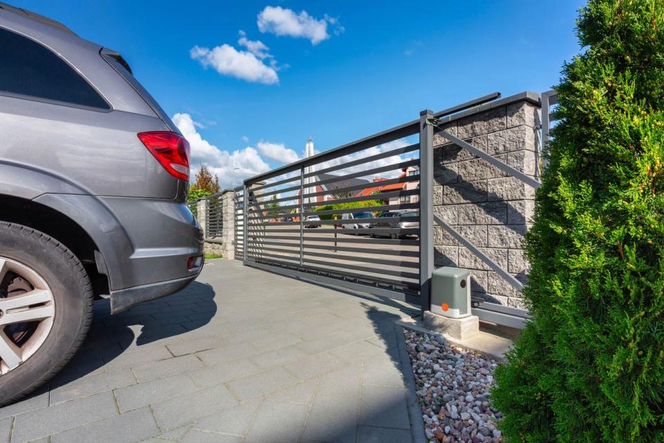 A silver car is parked in a driveway with the gate closed behind it.