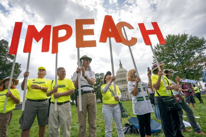 反對川普的美國民眾在國會山莊旁高舉「彈劾」（IMPEACH）的標語，以示抗議。（美聯社）