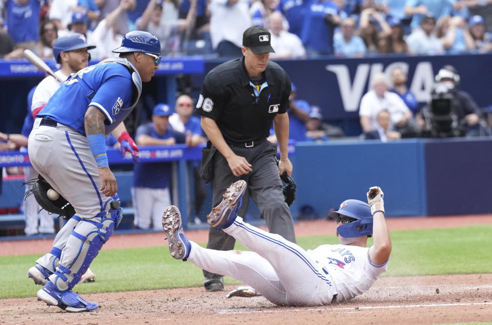 Toronto Blue Jays second baseman Davis Schneider scores on a wild pitch as Kansas City Royals catcher Salvador Perez and umpire Chris Segal look on during the sixth inning of a baseball game in Toronto on Sunday, Sept. 10, 2023. (Nathan Denette/The Canadian Press via AP)