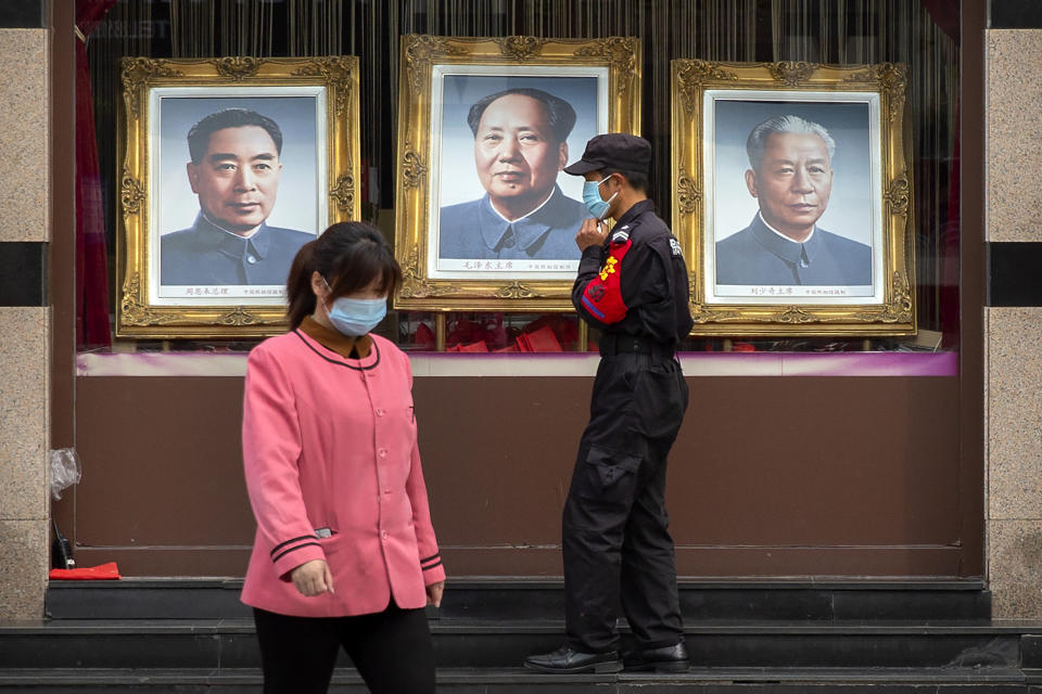 A security guard and worker wearing face masks to protect against the spread of the new coronavirus walk past portraits of Chinese leaders, from left, Zhou Enlai, Mao Zedong, and Liu Shaoqi in the window of a photo studio in Beijing, Wednesday, April 15, 2020. China reported several dozen new coronavirus cases on Wednesday, mostly from overseas. (AP Photo/Mark Schiefelbein)