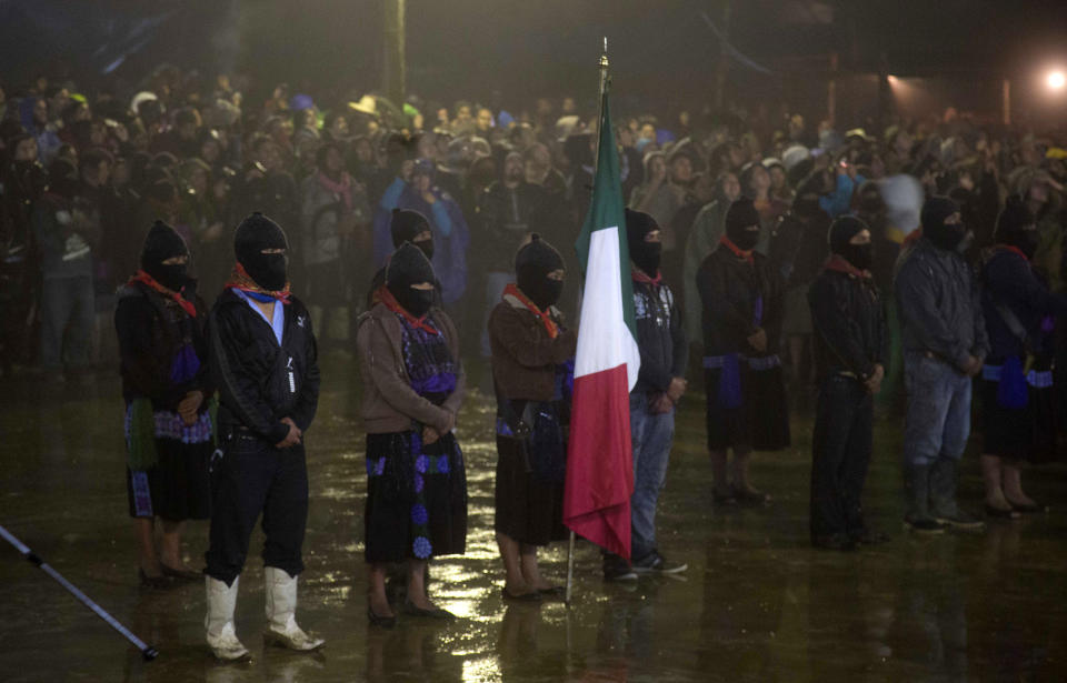 Masked members of the Zapatista National Liberation Army, EZLN, stand at attention, one holding Mexico's national flag, at an event marking the 20th anniversary of the Zapatista uprising in the town of Oventic, Chiapas, Mexico, late Tuesday, Dec. 31, 2013. The Zapatistas waged a brief armed uprising in the name of Indian rights in January of 1994. Since then, the rebels have waged a relatively peaceful resistance from the jungles of Chiapas. (AP Photo/Eduardo Verdugo)